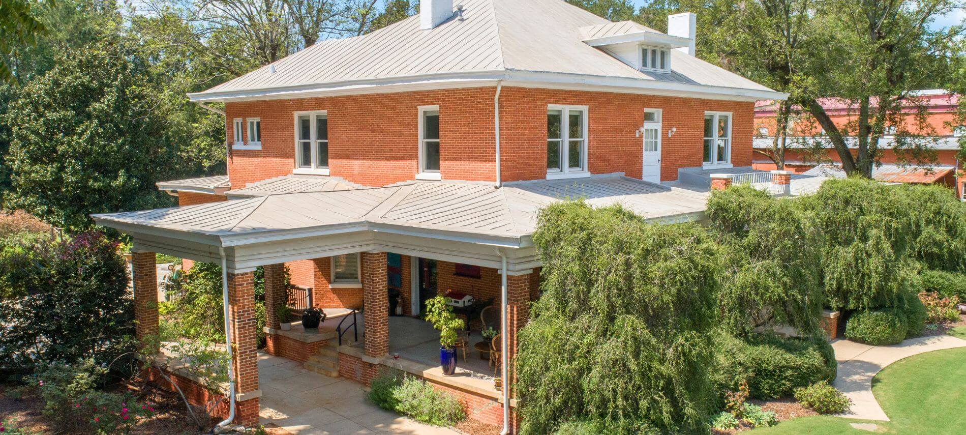 Historic red brick exterior of The Gillen House Bed and Breakfast surrounded by gardens and mature trees in Georgia.